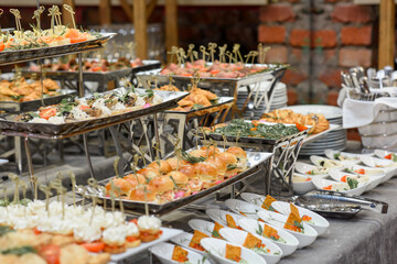 A set of canapes and snack at a banquet with white table. Slices of tomato, olive, cheese, bread and fish on food stand