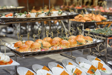 A set of canapes and snack at a banquet with white table. Slices of tomato, olive, cheese, bread and fish on food stand