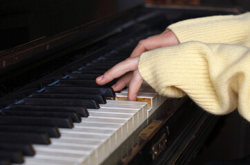 children hands in wool sweater sleeves playing on piano