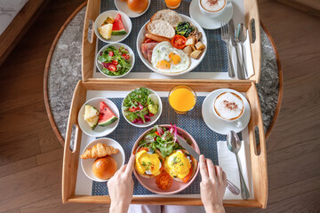Top View of Woman Hands Take Fork and Knife, Prepare to Eating Her Breakfast in Hotel. Room Service in Resort - Tasty Breakfast for Two with Fresh Eggs Benedict, Green Salad and Cup of Coffee