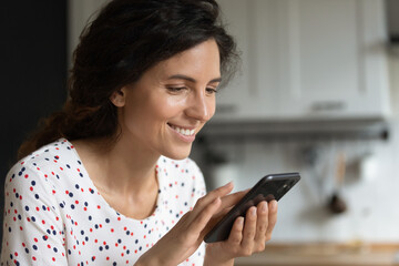 Happy Hispanic woman using apps and services on mobile phone at home, making quick payment, texting on social media chats, reading articles, shopping online on stores, watching videos on gadget