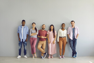 Portrait of a group of smiling multiracial people standing in a row on a light wall background....