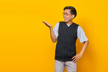 Portrait of smiling handsome young man showing copy space in palm on yellow background