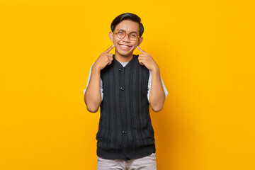 Portrait of smiling Asian young man with two fingers pointing dimples over yellow background