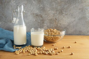 Vegan soy milk in a bottle and a drinking glass and soybeans in a bowl on a wooden table against a...