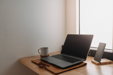 Laptop workspace on wooden desk by the windows with morning light.