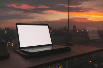 Laptop on wooden desk at the balcony with evening sunset city view.