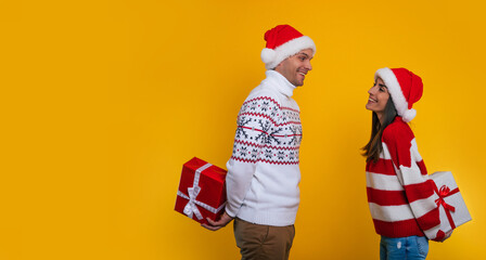 Happy excited young couple in love in Christmas clothes while they standing and hiding presents from each other behind back