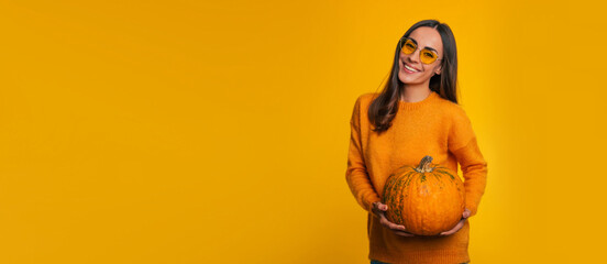 Banner photo of cute smiling young girl in eyeglasses with ripe pumpkin in hands while she is...