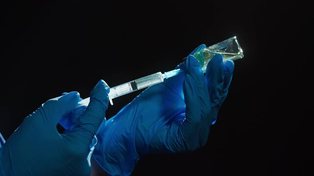Doctor filling syringe with solution on black background. Nurse wearing protective gloves showing sample of medicine, vaccination against covid-19, laboratory research concept. Coronavirus vaccine.