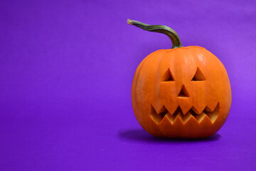 Halloween pumpkin with horror face, on purple background.