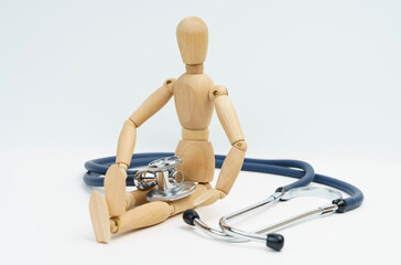 A wooden man sits on a white background, next to him and on him is a stethoscope.