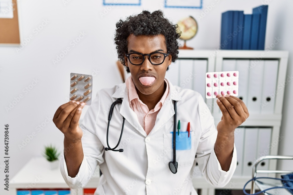 Canvas Prints african man wearing doctor uniform holding prescription pills sticking tongue out happy with funny e