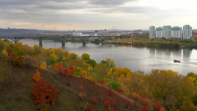 Autumn city. The microdistrict is built on the river bank next to the bridge. A ship on the river. Yellow, red trees