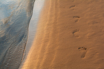 One human footprints on the beach sand in the evening sunset time. Footprints leading away from the viewer