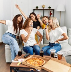 Group of young woman friends having party eating italian pizza and singing song at home.