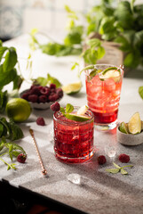Raspberry cocktail with lime,mint,ice cubes and fresh berries on grey background with juicy summer greenery.Beautiful photo of refreshing drink.