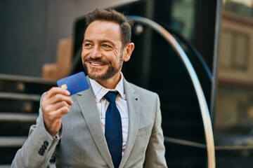 Middle age businessman smiling happy holding credit card at the city.