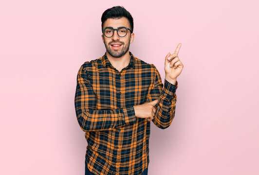 Hispanic man with beard wearing casual clothes and glasses smiling happy pointing with hand and finger to the side