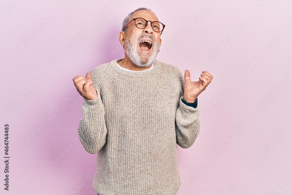 Sticker Handsome senior man with beard wearing casual sweater and glasses crazy and mad shouting and yelling with aggressive expression and arms raised. frustration concept.