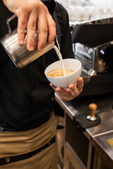 Professional barista pouring steamed milk into coffee glass cup making beautiful latte art Rosetta pattern in cafe. Flowing fresh ground coffee. Drinking roasted black coffee in the morning.