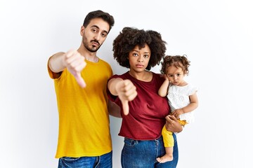 Interracial young family of black mother and hispanic father with daughter looking unhappy and angry showing rejection and negative with thumbs down gesture. bad expression. - Powered by Adobe