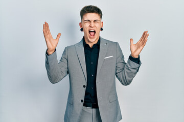 Young caucasian boy with ears dilation wearing business jacket celebrating mad and crazy for success with arms raised and closed eyes screaming excited. winner concept