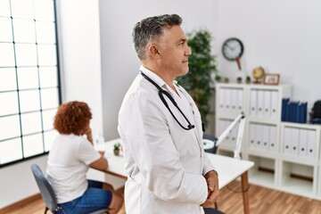 Middle age doctor man at the clinic with a patient looking to side, relax profile pose with natural face with confident smile.