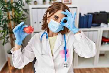 Fototapeta na wymiar Middle age doctor woman wearing safety mask holding virus toy smiling happy doing ok sign with hand on eye looking through fingers