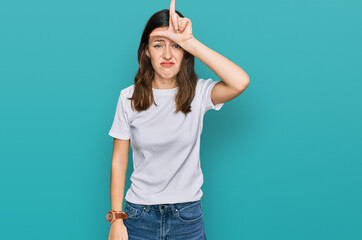 Young beautiful woman wearing casual white t shirt making fun of people with fingers on forehead doing loser gesture mocking and insulting.