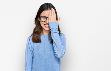 Young beautiful woman wearing casual clothes and glasses covering one eye with hand, confident smile on face and surprise emotion.