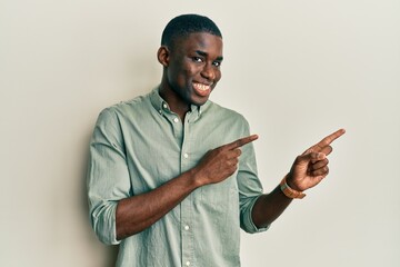 Naklejka premium Young african american man wearing casual clothes smiling and looking at the camera pointing with two hands and fingers to the side.