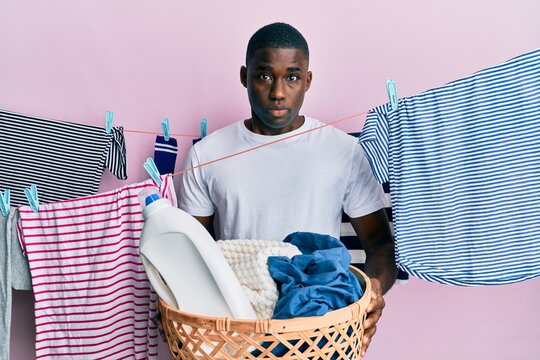 Young African American Man Holding Laundry Basket Clueless And Confused Expression. Doubt Concept.