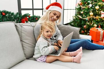 Mother and daughter using laptop sitting by christmas tree at home