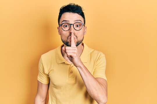 Young hispanic man wearing casual clothes and glasses asking to be quiet with finger on lips. silence and secret concept.