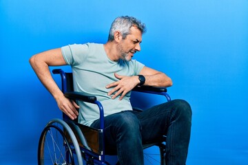 Handsome middle age man with grey hair sitting on wheelchair suffering of backache, touching back with hand, muscular pain