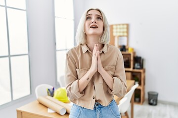 Young beautiful caucasian woman at construction office begging and praying with hands together with hope expression on face very emotional and worried. begging.