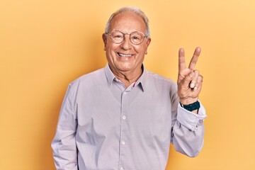 Senior man with grey hair wearing elegant shirt and glasses smiling with happy face winking at the camera doing victory sign. number two.