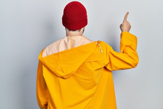 Caucasian man with beard wearing yellow raincoat posing backwards pointing ahead with finger hand