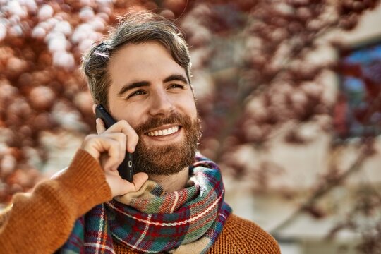 Caucasian man with beard having a conversation speaking on the phone outdoors on a sunny day