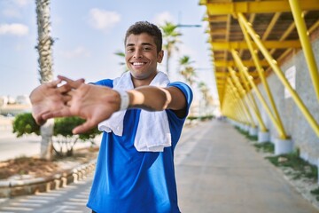 Young hispanic man stretching arms muscles outdoors