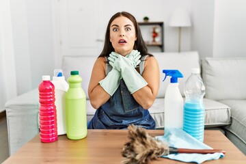 Young brunette woman wearing cleaner apron and gloves cleaning at home shouting and suffocate because painful strangle. health problem. asphyxiate and suicide concept.