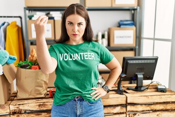 Young brunette woman wearing volunteer t shirt at donations stand doing italian gesture with hand...