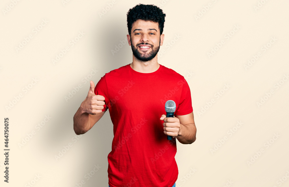 Poster Young arab man with beard singing song using microphone smiling happy and positive, thumb up doing excellent and approval sign