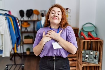 Young redhead woman working as manager at retail boutique smiling with hands on chest with closed eyes and grateful gesture on face. health concept.