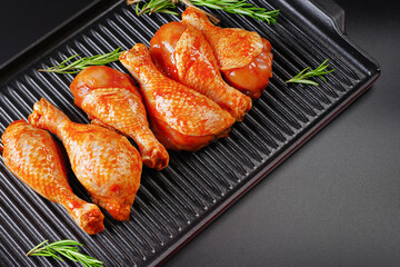 Raw chicken drumstick with spices and green rosemary on a black background .Marinated chicken dramstick on a grill pan with spices for cooking.