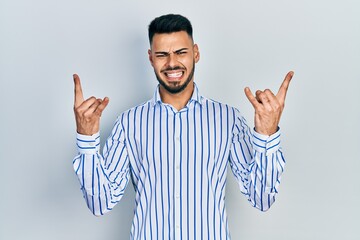 Naklejka premium Young hispanic man with beard wearing casual striped shirt shouting with crazy expression doing rock symbol with hands up. music star. heavy concept.