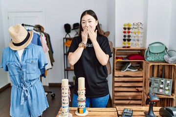 Young asian woman working as manager at retail boutique laughing and embarrassed giggle covering...