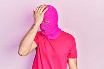 Young hispanic man with modern dyed hair wearing pink balaclava mask face surprised with hand on...
