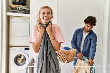Young couple smiling happy doing laundry. Woman smelling clean clothes at home.